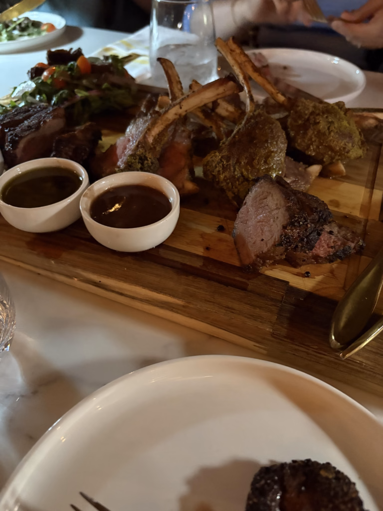 A picture of the "Large Meat Board" at Lamppost Bistro which includes: 1 Bone-In Rib Steak, 2 Fillet Mignon, 1 Lamb Chops, 1 Skirt Steak Salad, Tri-color Sweet Potato Fries, House Fries, Onion Rings